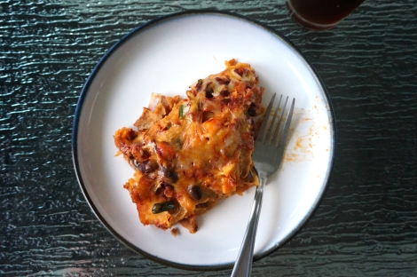 A serving of sweet potato-black bean enchiladas sits on a small plate, with one bite already taken and a fork lying where the bite had been.