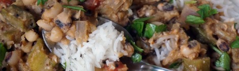 Closeup on a spoon of black-eyed pea and okra curry, with rice, sitting in the midst of the larger plateful, the delicate white grains of rice contrasting with the hearty thickness of brown, red, olive, and green curry ingredients.
