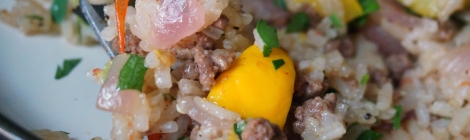 A bite of pilaf on a fork in close-up, bits of ground beef, onion, parsley, and tomato scattered among the grains of rice, and a bright yellow chunk of squash dead center.