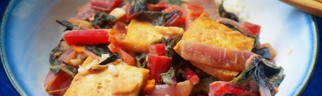 Closeup on a bowl of tofu and chard, the bright red of the chard stems standing out against the rich gold-brown of the fried tofu squares and the dark green of the chard leaves.